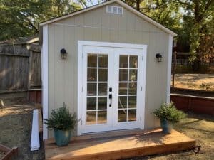 Garden shed with double glass doors, outdoor potted plants, and wooden deck.
