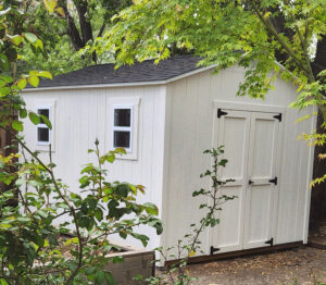 White shed surrounded by greenery.